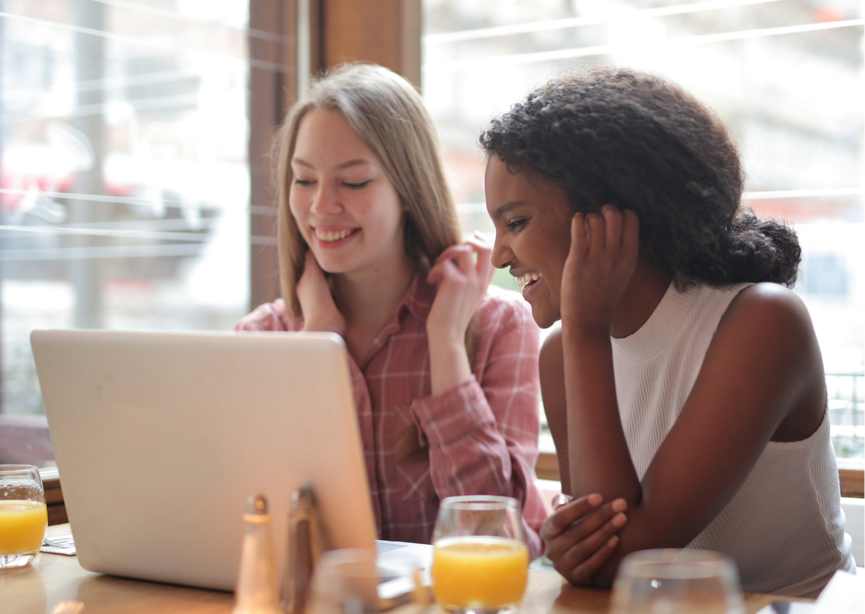 Lady with pink checked shirt and lady with white tank top looking at the laptop together